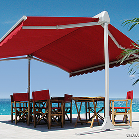 Eine rote freistehende Markise, die ebenfalls rote Stühle und einen Tisch beschattet, vor türkis-blauem Meer.