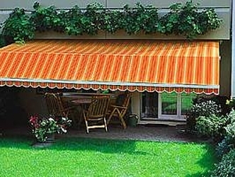 Frotansicht einer orangen Gelenkarmmarkise mit Knick über einer Terrasse und Wiese.