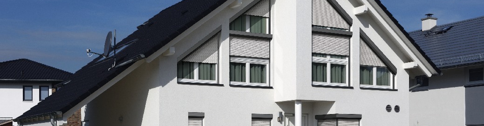 Frontansicht eines weißen Einfamilienhauses, mit einigen Rolladen und Schräg-Rolladen an den Fenstern