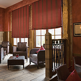 rot-braune, halb-geöffnete Raffrollos in einem Wohnzimmer, eingerichtet fast ausschließlich mit Holz.